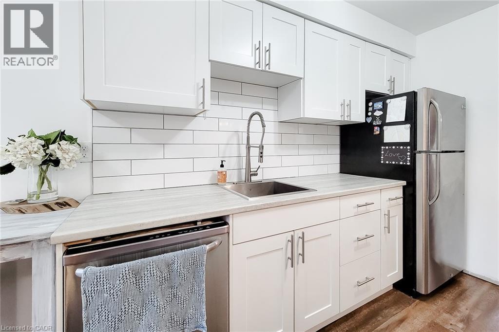 Modern kitchen featuring white shaker cabinetry with brushed nickel hardware, light-toned countertops, a subway tile backsplash, stainless steel sink with a gooseneck faucet, and a stainless steel ref - 7 Davidson Boulevard Unit# 14, Dundas, ON - Indoor Photo Showing Kitchen With Upgraded Kitchen