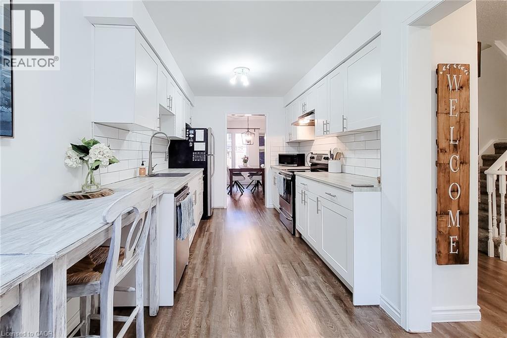 Galley kitchen featuring white cabinetry, subway tile backsplash, wood-finish flooring, a stainless steel sink with a gooseneck faucet, and a breakfast bar - 7 Davidson Boulevard Unit# 14, Dundas, ON - Indoor Photo Showing Kitchen