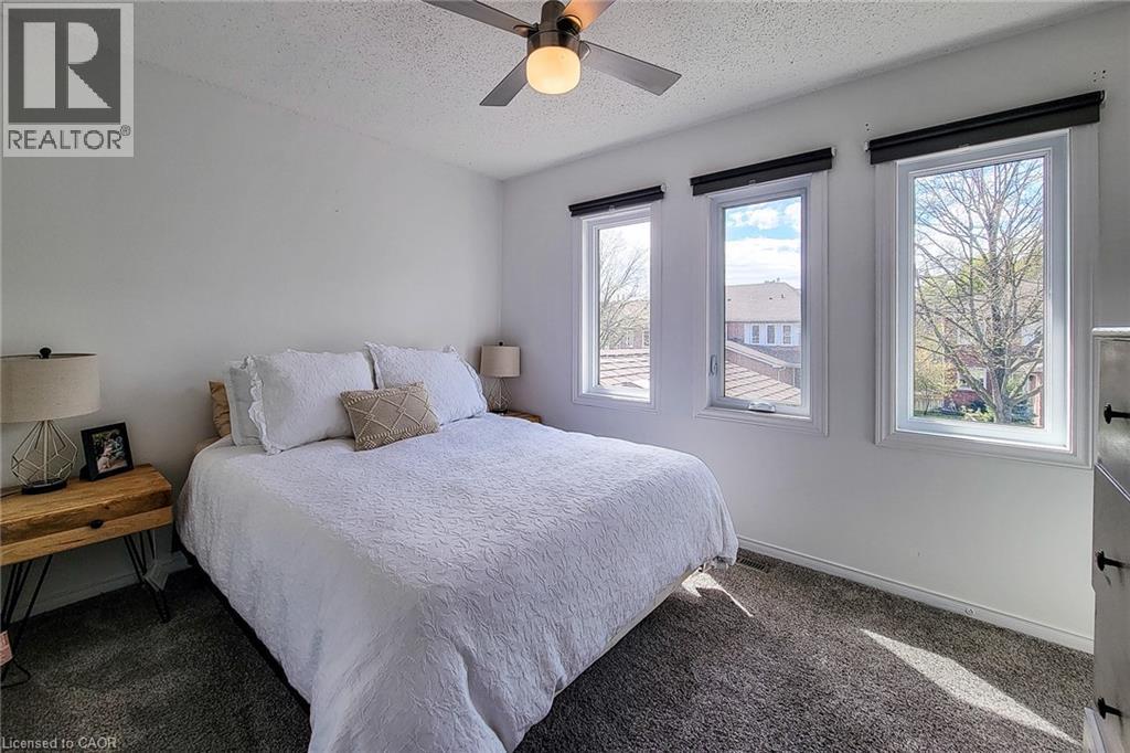Spacious room featuring three large windows, a ceiling fan, plush carpet flooring, and neutral wall tones - 7 Davidson Boulevard Unit# 14, Dundas, ON - Indoor Photo Showing Bedroom