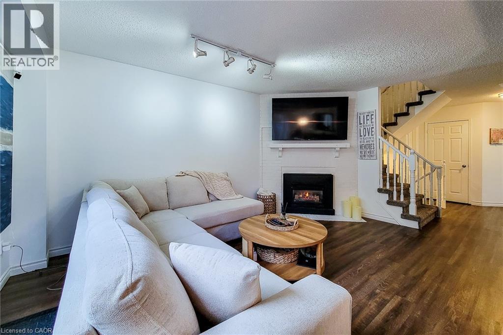 Living area with wood-finish flooring, a fireplace featuring a white brick surround, and an integrated mantel - 7 Davidson Boulevard Unit# 14, Dundas, ON - Indoor Photo Showing Living Room With Fireplace