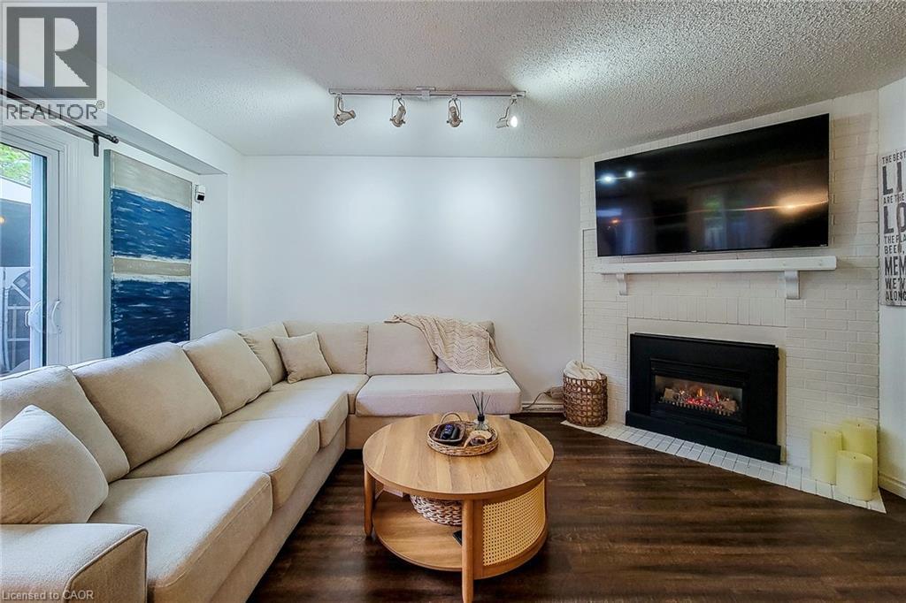 Living area featuring wood-finish flooring and a white brick-style fireplace with a black insert - 7 Davidson Boulevard Unit# 14, Dundas, ON - Indoor Photo Showing Living Room With Fireplace