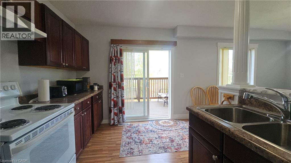 Kitchen featuring a double stainless steel sink, wood-finish flooring, dark wood cabinetry, light-colored countertops, and a sliding glass door leading to an outdoor deck - 10 Doll Court, Kitchener, ON - Indoor Photo Showing Kitchen With Double Sink