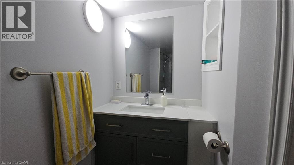 Bathroom vanity featuring a single sink with a chrome faucet, light-toned countertop, and dark cabinetry - 10 Doll Court, Kitchener, ON - Indoor Photo Showing Bathroom