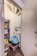 Dedicated laundry closet featuring a stacked washer and dryer unit, wood-finish flooring, and built-in shelving -