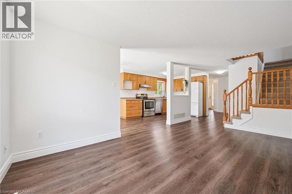 Spacious interior featuring wood-finish flooring, white walls, and a visible kitchen with wood cabinetry and stainless steel appliances - 71 Peach Blossom Crescent, Kitchener, ON - Indoor
