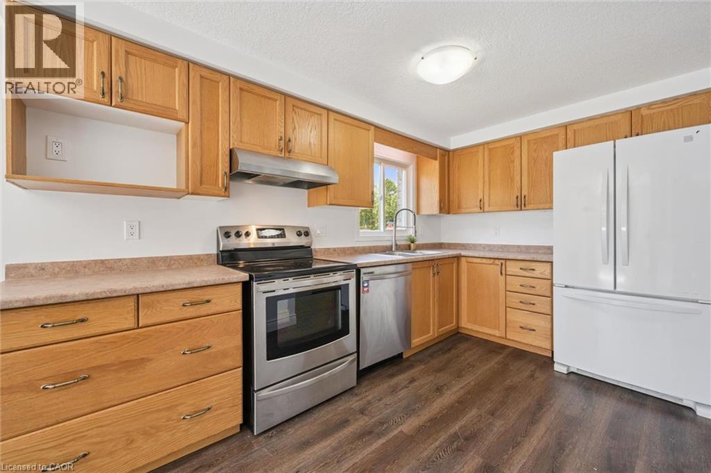 Corner kitchen featuring wood cabinetry, dark wood-finish flooring, a stainless steel range with overhead ventilation, a stainless steel dishwasher, and a white refrigerator - 71 Peach Blossom Crescent, Kitchener, ON - Indoor Photo Showing Kitchen
