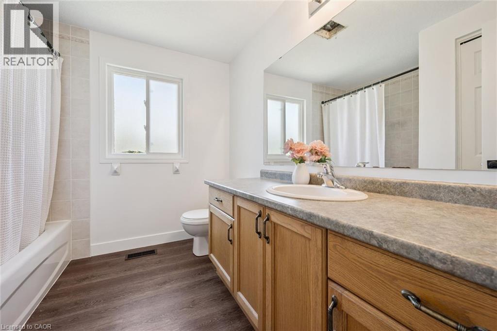 Bathroom featuring wood-finish flooring, a single vanity with light wood cabinetry, a built-in sink, and a large mirror - 71 Peach Blossom Crescent, Kitchener, ON - Indoor Photo Showing Bathroom