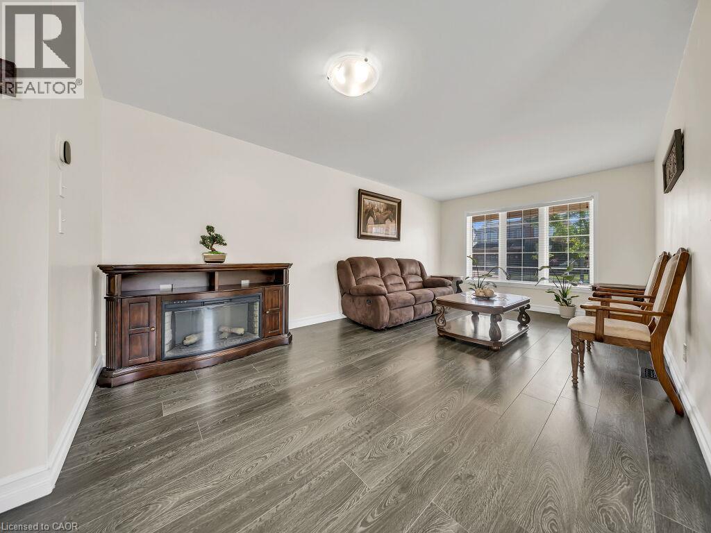Spacious living area featuring wood-finish flooring, an electric fireplace media console, and a large multi-pane window - 39 Baintree Way, Cambridge, ON - Indoor Photo Showing Living Room