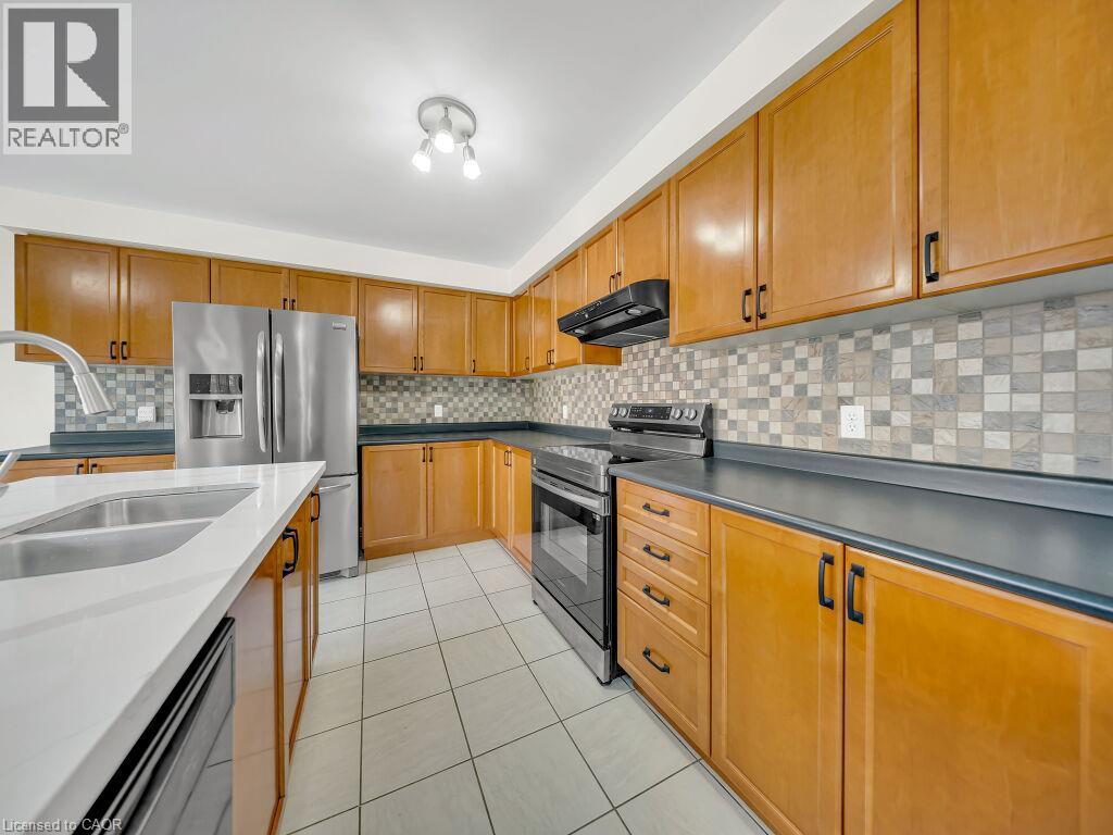 Kitchen featuring abundant wood cabinetry, stainless steel appliances, dark countertops, a mosaic tile backsplash, and white tile flooring - 39 Baintree Way, Cambridge, ON - Indoor Photo Showing Kitchen With Stainless Steel Kitchen With Double Sink