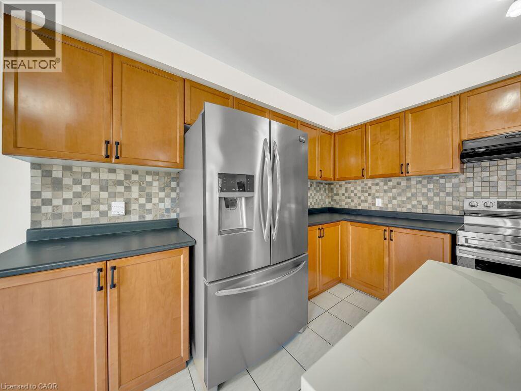 Kitchen featuring light wood-finish cabinetry, dark countertops, and a mosaic tile backsplash - 39 Baintree Way, Cambridge, ON - Indoor Photo Showing Kitchen