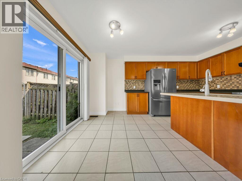 Kitchen area with light-toned tile flooring, honey-toned cabinetry, and dark countertops - 39 Baintree Way, Cambridge, ON - Indoor Photo Showing Kitchen