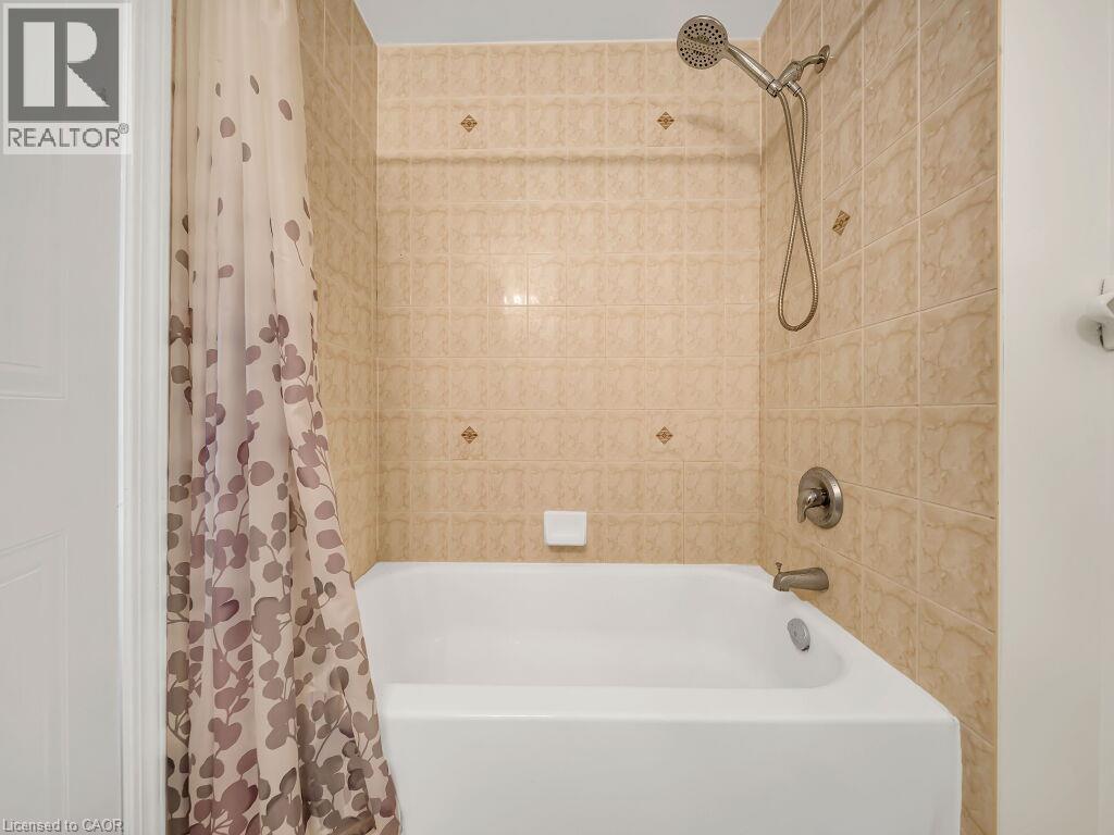 White bathtub with brushed nickel fixtures, surrounded by beige patterned wall tiles and decorative accent tiles - 39 Baintree Way, Cambridge, ON - Indoor Photo Showing Bathroom
