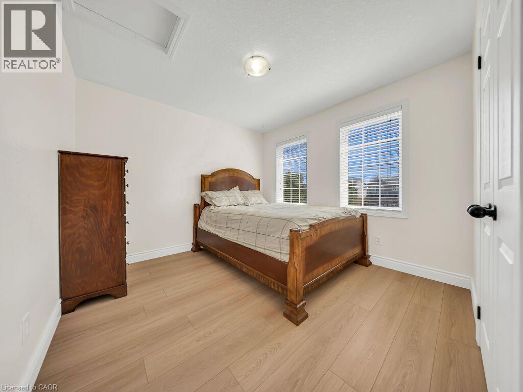 Light-filled room featuring two windows with horizontal blinds, light wood-finish flooring, a ceiling-mounted light fixture, and white trim - 39 Baintree Way, Cambridge, ON - Indoor Photo Showing Bedroom