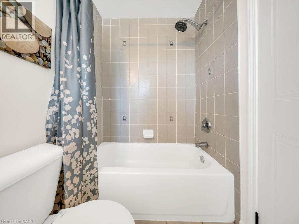 Bathroom featuring a white bathtub with chrome fixtures, tan square wall tiling, and a white toilet - 39 Baintree Way, Cambridge, ON - Indoor Photo Showing Bathroom