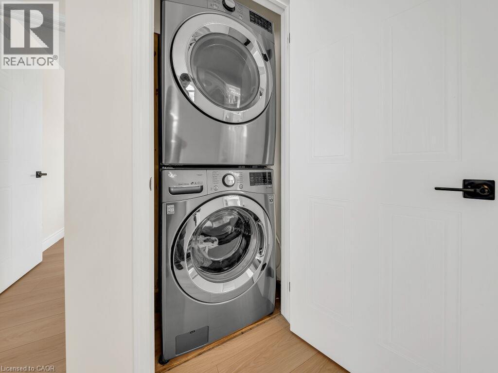 Dedicated laundry closet featuring a stacked washer and dryer, white paneled doors, black hardware, and wood-finish flooring - 39 Baintree Way, Cambridge, ON - Indoor Photo Showing Laundry Room