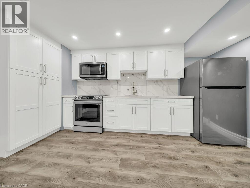 Modern kitchen featuring white shaker cabinetry, stainless steel appliances, light countertops, a marble-patterned backsplash, and wood-finish flooring - 39 Baintree Way, Cambridge, ON - Indoor Photo Showing Kitchen