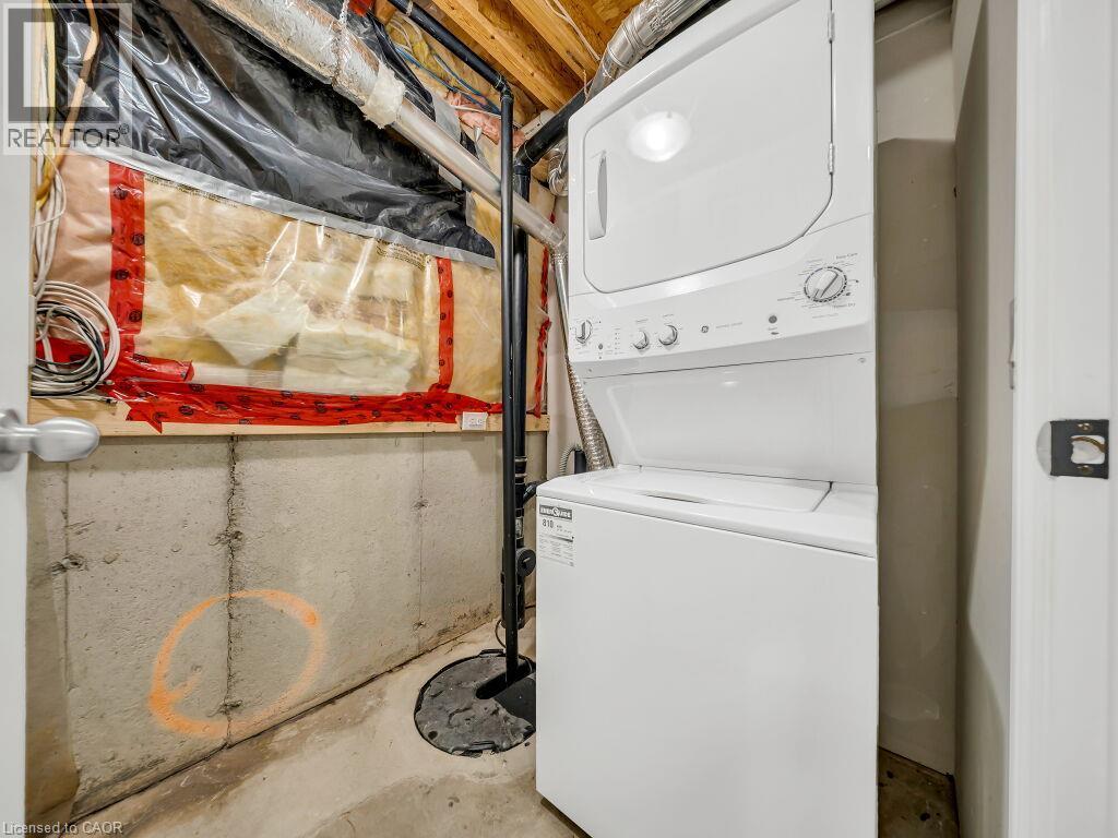 Dedicated utility area featuring a white stackable washer and dryer unit, concrete foundation walls, exposed overhead ductwork, and a visible sump pump - 39 Baintree Way, Cambridge, ON - Indoor Photo Showing Laundry Room