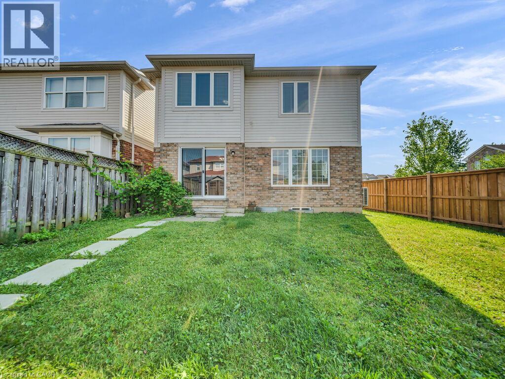 Rear exterior featuring a spacious lawn, brick and siding facade, multiple windows, and a sliding glass door - 39 Baintree Way, Cambridge, ON - Outdoor