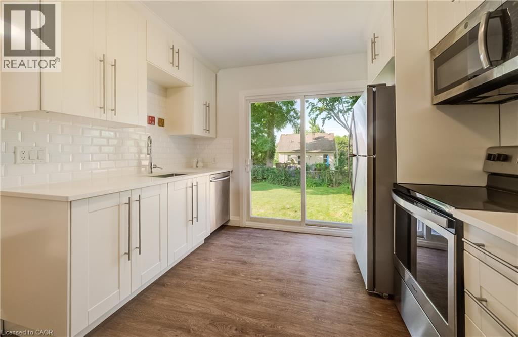 Kitchen featuring white cabinetry, light countertops, subway tile backsplash, and wood-finish flooring - 55 Rex Drive, Kitchener, ON - Indoor Photo Showing Kitchen