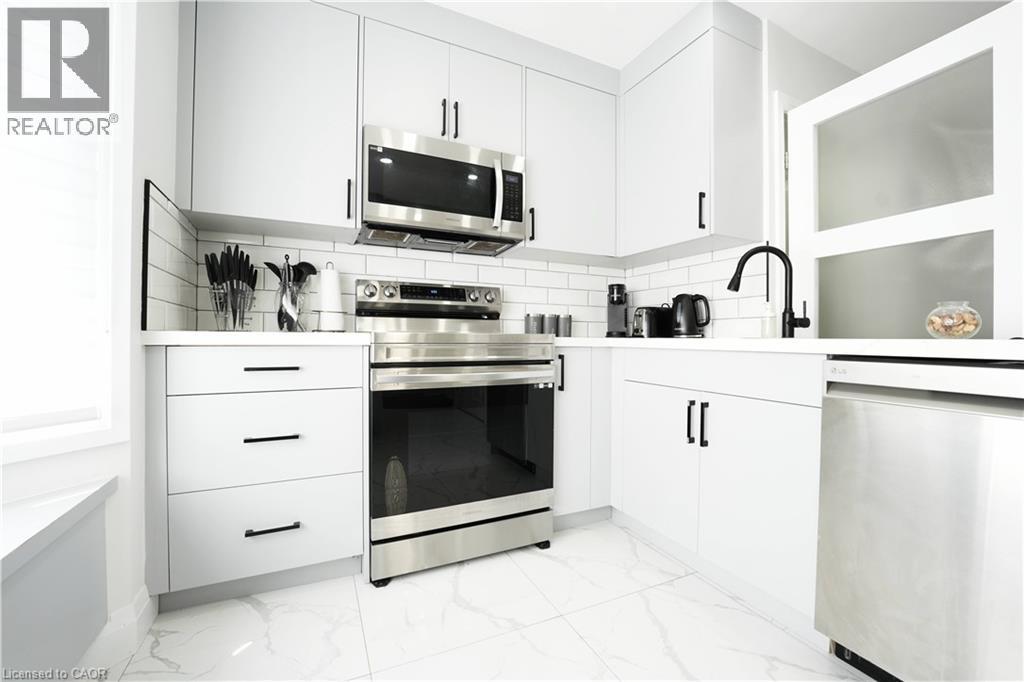 Modern kitchen featuring white cabinetry with matte black hardware, stainless steel appliances, white subway tile backsplash, white countertops, and large format tile flooring - 136 Jansen Avenue, Kitchener, ON - Indoor Photo Showing Kitchen
