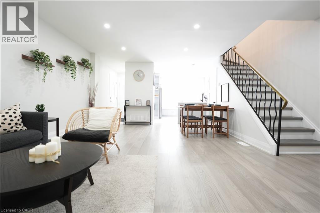 Open-concept living area featuring light wood-finish flooring, recessed lighting, a modern staircase with a black wrought iron railing and brass handrail, and a dining area with built-in countertop se - 136 Jansen Avenue, Kitchener, ON - Indoor Photo Showing Living Room