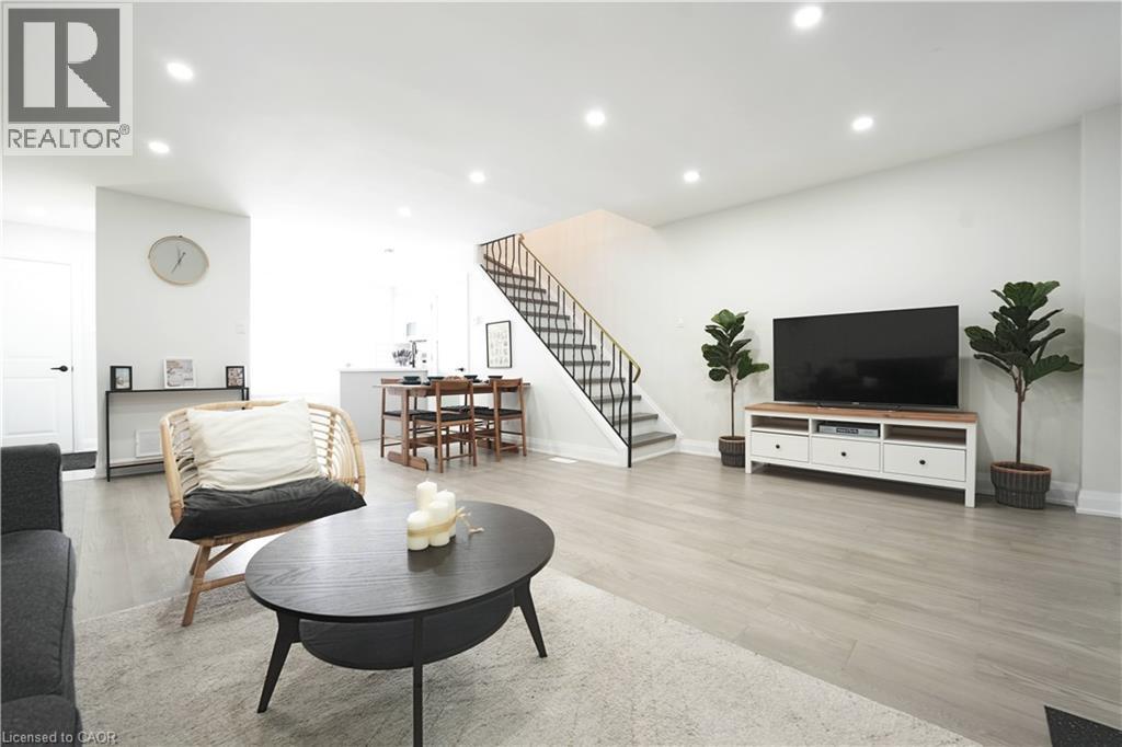 Open-concept living area featuring light wood-finish flooring, recessed lighting, white walls, a dining area, and a staircase with a black metal railing - 136 Jansen Avenue, Kitchener, ON - Indoor Photo Showing Living Room