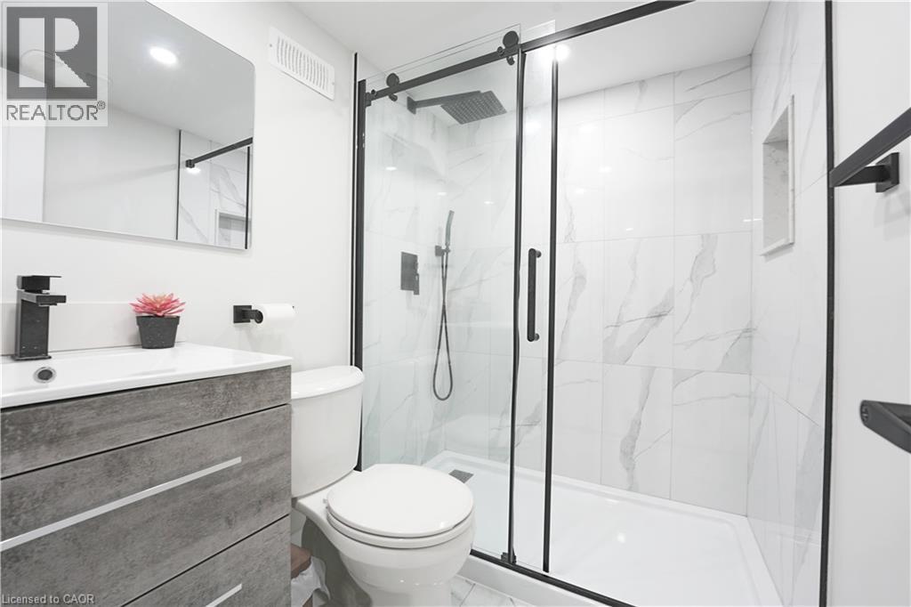 Bathroom featuring a frameless glass shower enclosure with matte black hardware, white marble-look tile, a built-in shower niche, and a vanity with a rectangular sink and matte black faucet - 136 Jansen Avenue, Kitchener, ON - Indoor Photo Showing Bathroom