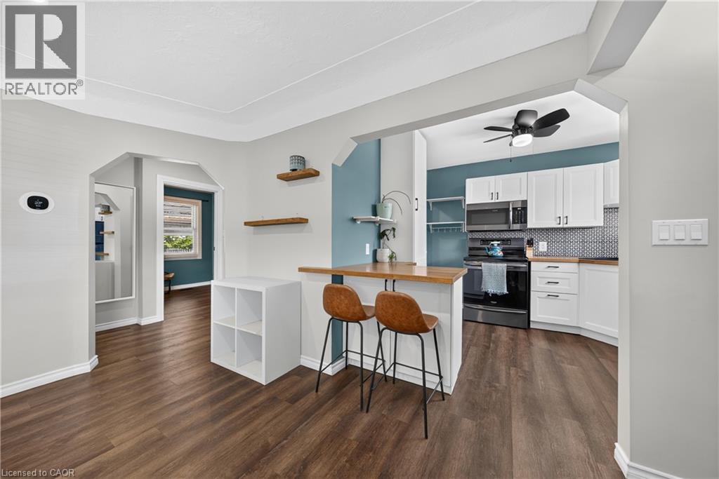 Open-concept layout featuring wood-finish flooring, arched doorways, and a kitchen with white cabinetry, a patterned tile backsplash, and dark appliances - 621 Tate Avenue, Hamilton, ON - Indoor Photo Showing Kitchen