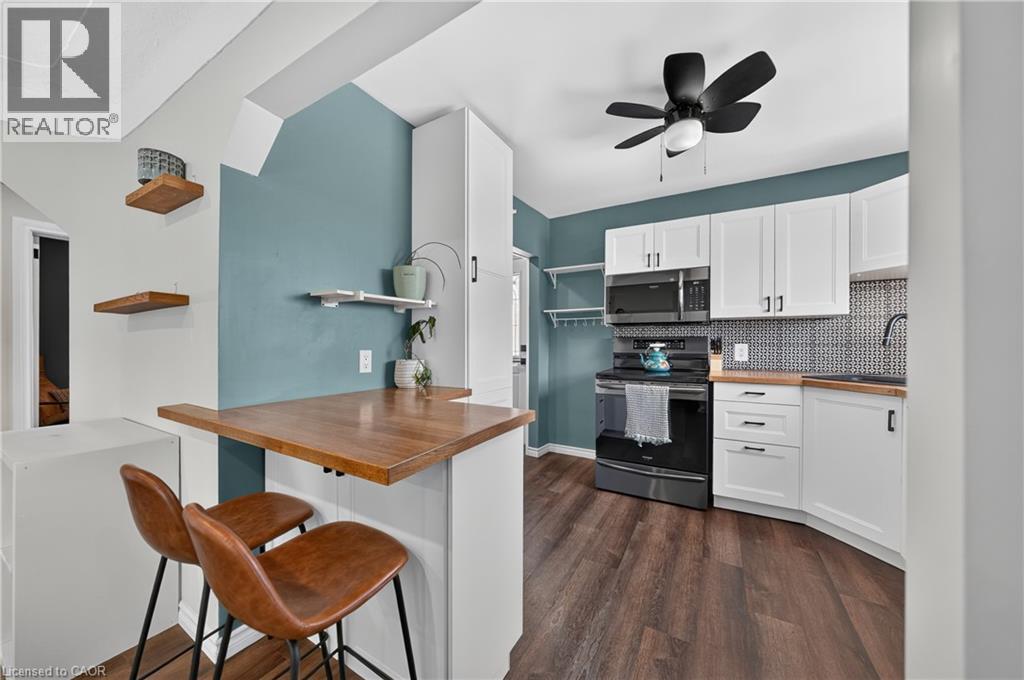 Contemporary kitchen featuring white cabinetry, wood-finish countertops, and a black appliance suite including a range and microwave - 621 Tate Avenue, Hamilton, ON - Indoor Photo Showing Other Room