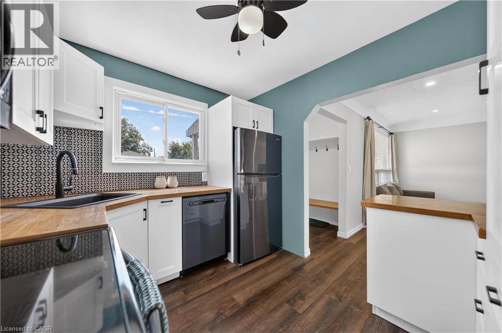 Kitchen featuring white cabinetry with matte black hardware, wood-finish countertops, and a patterned tile backsplash - 621 Tate Avenue, Hamilton, ON - Indoor Photo Showing Kitchen