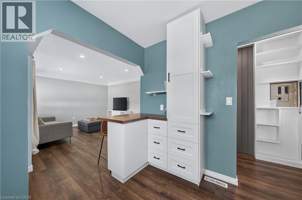 Wood-finish flooring throughout, featuring a peninsula with a wood-finish countertop, white cabinetry with black hardware, and an integrated tall cabinet - 621 Tate Avenue, Hamilton, ON - Indoor