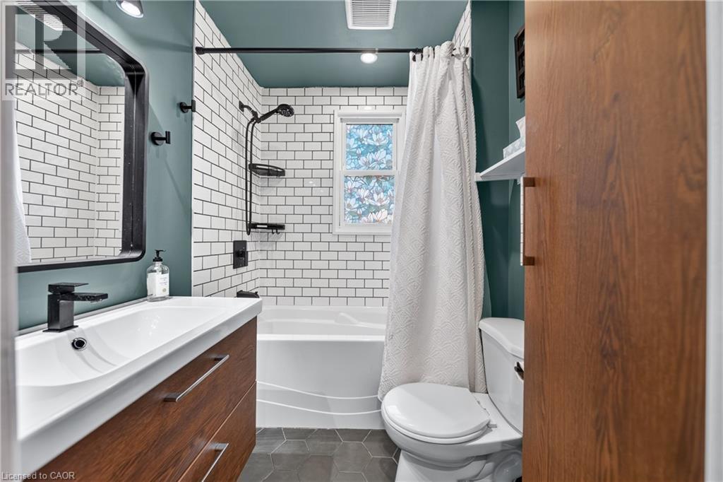 Bathroom featuring a wood-finish vanity with an integrated sink and matte black faucet, subway tile shower surround, and hexagonal floor tiles - 621 Tate Avenue, Hamilton, ON - Indoor Photo Showing Bathroom