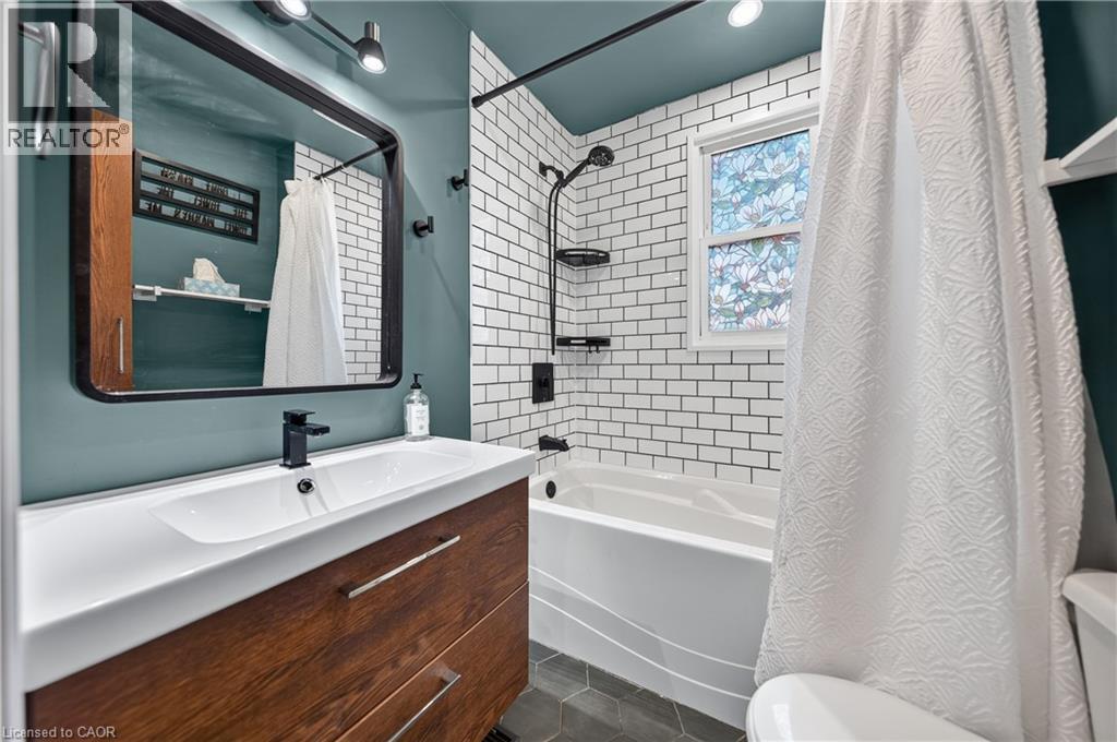 Bathroom featuring a wood-finish vanity with an integrated sink and matte black faucet, a framed mirror, subway tile shower surround, and a window with decorative glass - 621 Tate Avenue, Hamilton, ON - Indoor Photo Showing Bathroom
