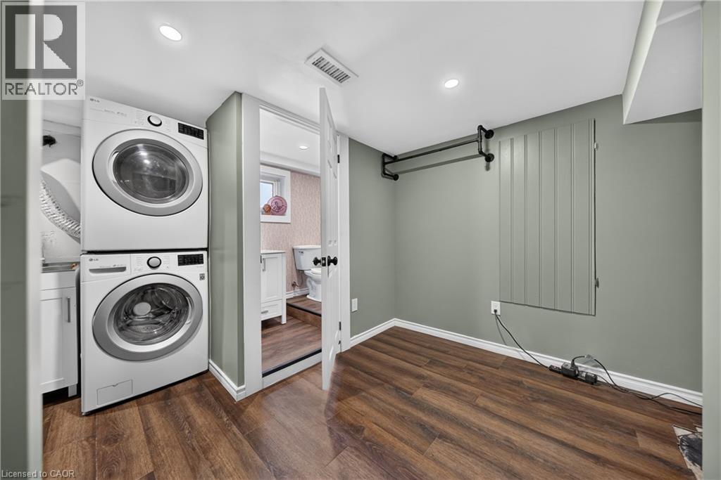 Dedicated laundry area featuring stacked appliances and wood-finish flooring - 621 Tate Avenue, Hamilton, ON - Indoor Photo Showing Laundry Room