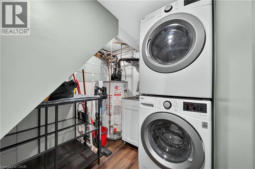Dedicated laundry area featuring a stacked washer and dryer unit, wood-finish flooring, and a utility sink with white cabinetry - 621 Tate Avenue, Hamilton, ON - Indoor Photo Showing Laundry Room