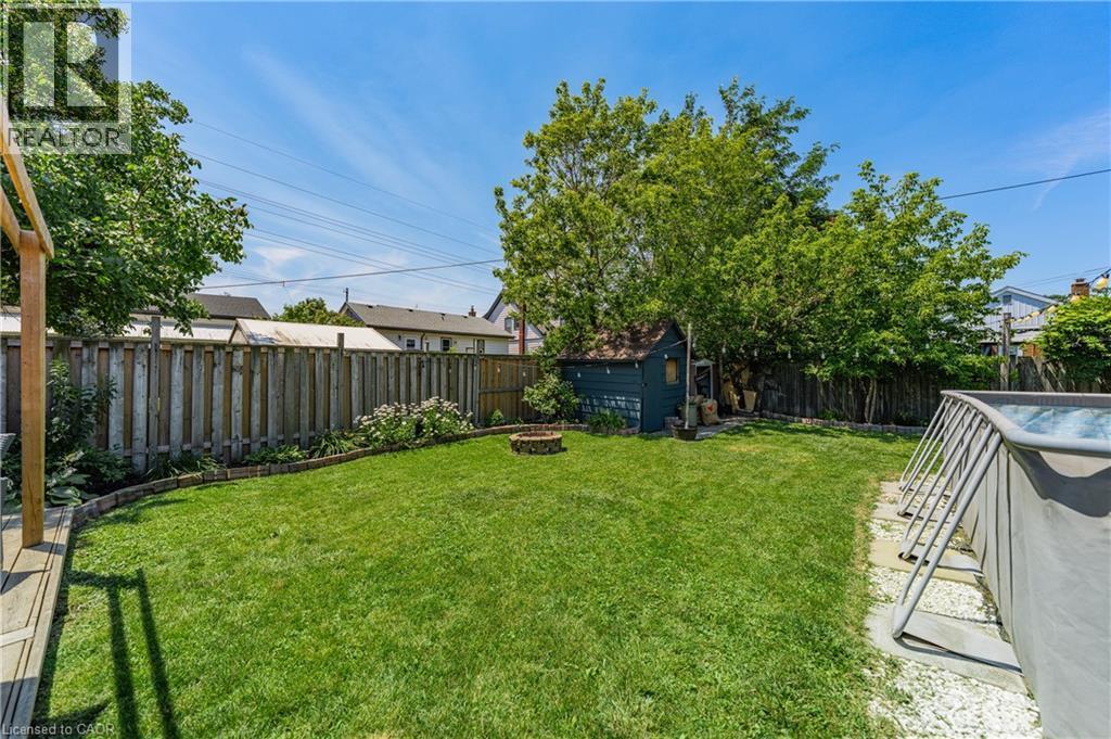 Expansive backyard featuring a lush lawn, wood fencing, a dedicated fire pit area, an outdoor shed, and mature trees providing natural screening - 621 Tate Avenue, Hamilton, ON - Outdoor With Backyard