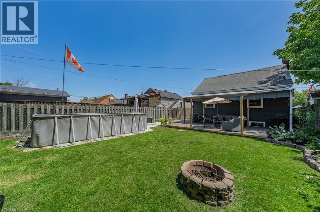 Expansive backyard featuring a manicured lawn, an above-ground pool, a stone-built fire pit, and a covered wooden deck - 621 Tate Avenue, Hamilton, ON - Outdoor