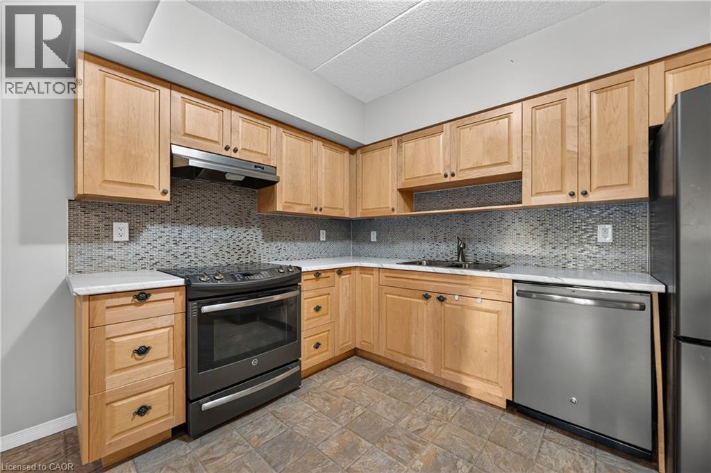 U-shaped kitchen with light wood-finish cabinetry, white countertops, and a mosaic tile backsplash - 155 Water Street S Unit# 203, Cambridge, ON - Indoor Photo Showing Kitchen With Stainless Steel Kitchen With Double Sink