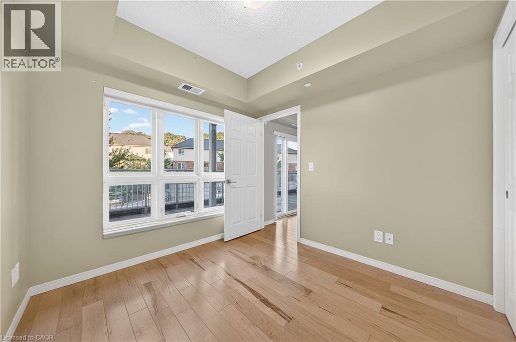 Room with wood-finish flooring, neutral wall paint, and a large multi-pane window - 155 Water Street S Unit# 203, Cambridge, ON - Indoor Photo Showing Other Room