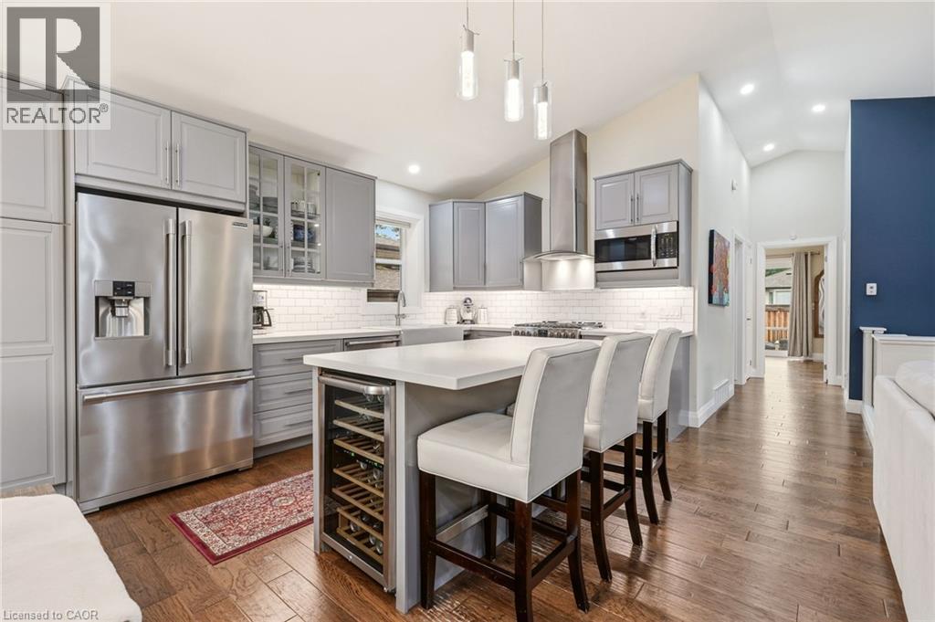 Modern kitchen featuring stainless steel appliances, grey cabinetry, a subway tile backsplash, and a central island with integrated wine refrigeration - 715 Drury Lane, Burlington, ON - Indoor