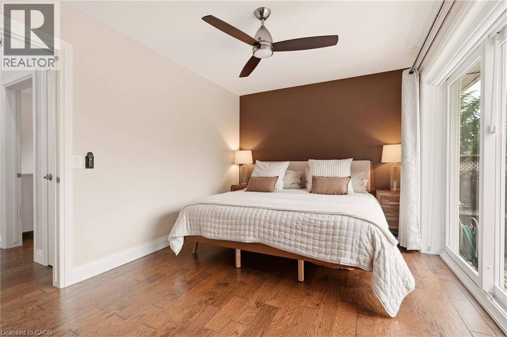 Wood-finish flooring throughout, featuring a distinctive accent wall, a modern ceiling fan, and large glass sliding doors providing exterior access - 715 Drury Lane, Burlington, ON - Indoor Photo Showing Bedroom