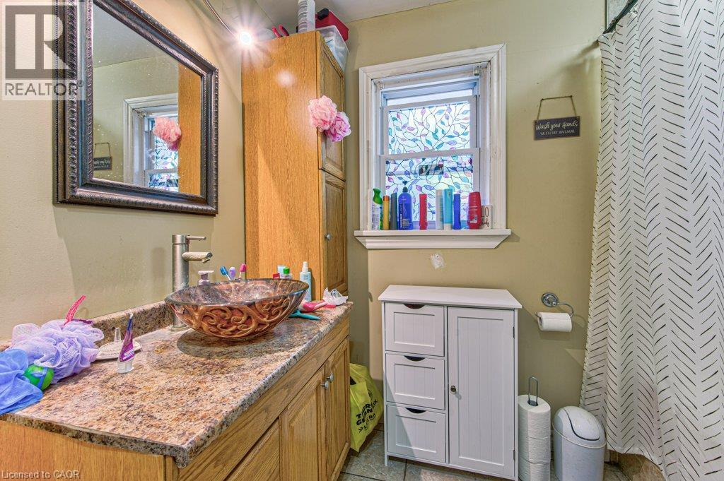 Bathroom featuring a vessel sink with an ornate glass basin, a vanity with a faux-granite countertop and wood-finish cabinetry, a framed mirror, and a wall-mounted storage cabinet - 819 Duke Street, Cambridge, ON - Indoor Photo Showing Bathroom