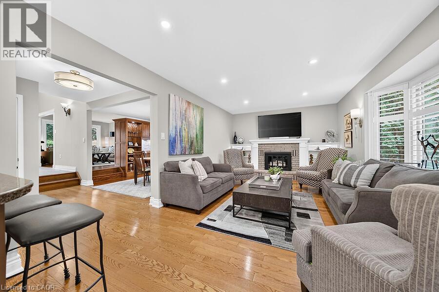 Spacious living area featuring hardwood-finish flooring, a brick fireplace with a white mantel, recessed lighting, and a bay window with plantation shutters - 30 Carriagegate Drive, Hamilton, ON - Indoor Photo Showing Living Room With Fireplace