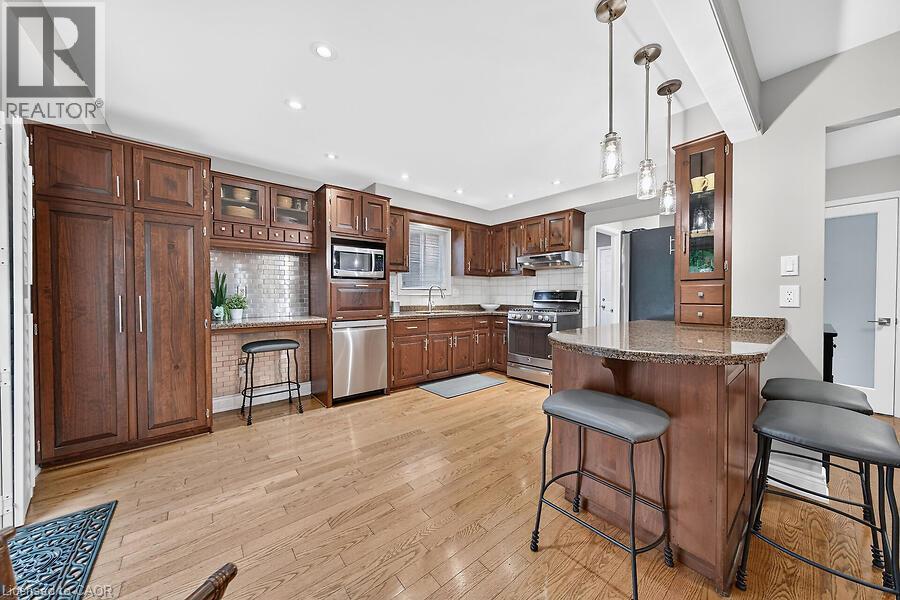 Kitchen featuring wood-finish flooring, dark wood cabinetry, stainless steel appliances, a stone countertop island with pendant lighting, and recessed ceiling lights - 30 Carriagegate Drive, Hamilton, ON - Indoor Photo Showing Kitchen