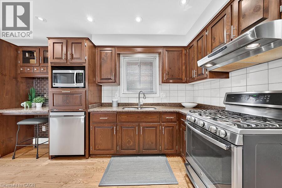 Kitchen featuring wood-finish cabinetry, granite-style countertops, stainless steel appliances, a tile backsplash, and wood-finish flooring - 30 Carriagegate Drive, Hamilton, ON - Indoor Photo Showing Kitchen With Stainless Steel Kitchen With Double Sink