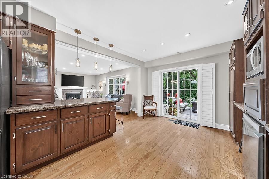 Open-concept kitchen featuring wood-finish flooring, dark wood cabinetry, a stone-finish countertop island, and recessed lighting - 30 Carriagegate Drive, Hamilton, ON - Indoor Photo Showing Kitchen