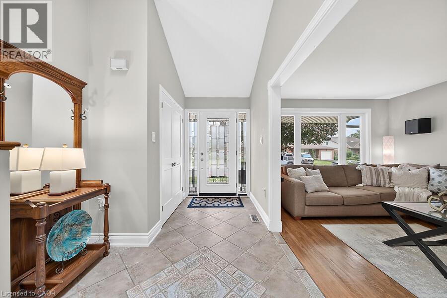 Inviting foyer with tile flooring and a bright glass-paneled entry door, opening to a living area featuring wood-finish flooring and a large window - 30 Carriagegate Drive, Hamilton, ON - Indoor Photo Showing Living Room