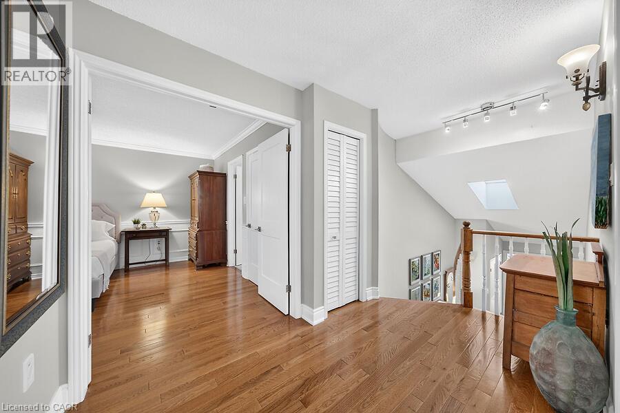 Hardwood flooring throughout the upper level landing, featuring a skylight, white louvered bifold doors, and painted wood railings - 30 Carriagegate Drive, Hamilton, ON - Indoor Photo Showing Other Room