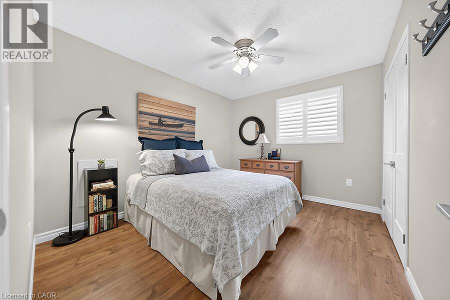 Bedroom featuring wood-finish flooring, a ceiling fan with integrated lighting, and a window with plantation shutters - 30 Carriagegate Drive, Hamilton, ON - Indoor Photo Showing Bedroom