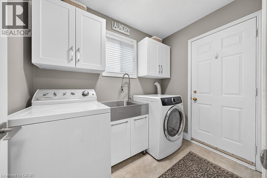 Laundry room featuring white cabinetry, a stainless steel utility sink with a high-arc faucet, and tiled flooring - 30 Carriagegate Drive, Hamilton, ON - Indoor Photo Showing Laundry Room